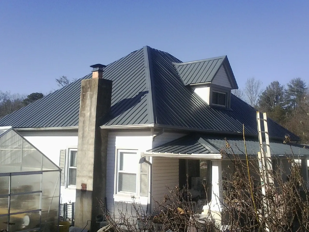Dark blue standing seam metal roof on a white farmhouse with dormer — Slate & Tile Roof Repair by Roofing Brothers in Edmeston