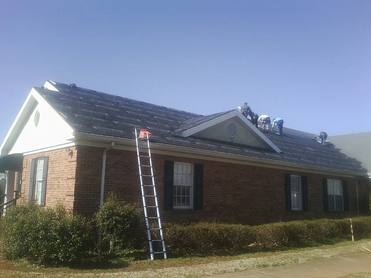 Crew tearing shingles off a brick ranch roof with a ladder set — Emergency Roof Repair work by our crew in Edmeston