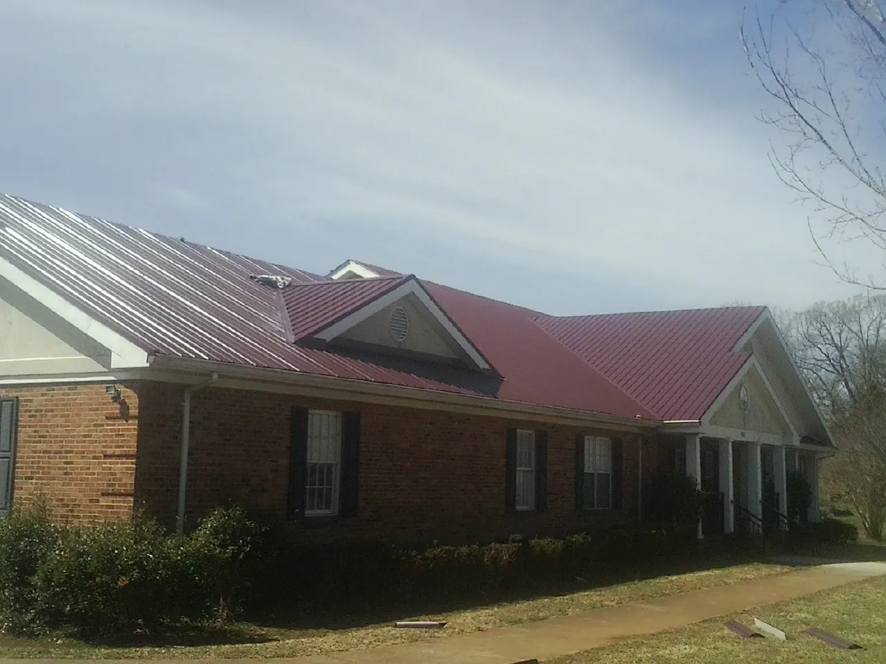 Red metal roof with gabled entries on a long brick building, from a Hail Damage Roof Repair job in Edmeston
