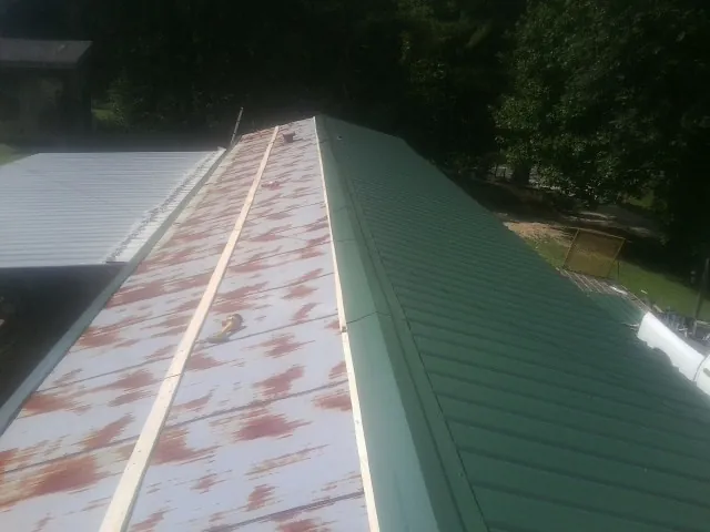 Old rusted panels beside newly installed green metal roofing — Wind Damage Roof Repair by Roofing Brothers in Edmeston