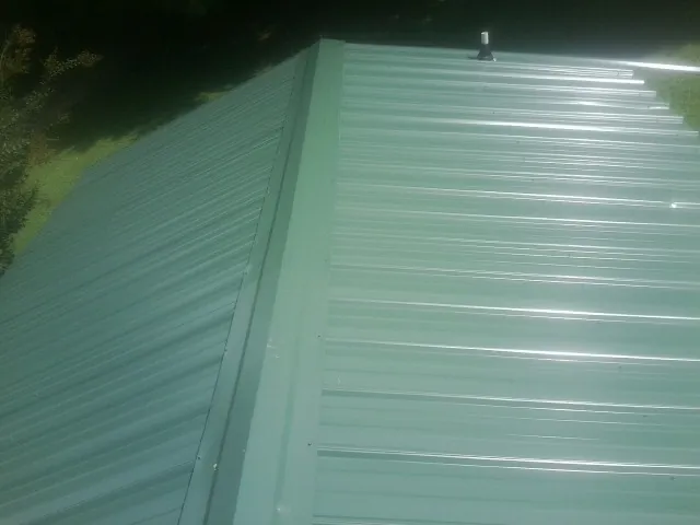 New green metal panels meeting at the ridge of a roof — Flat Roof Repair work by our crew in Edmeston
