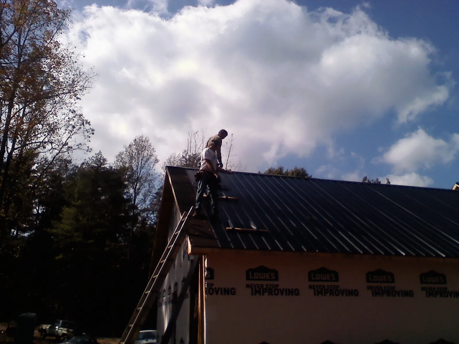 Roofer fastening dark metal panels high against a cloudy sky, from a Roof Inspection job in Edmeston
