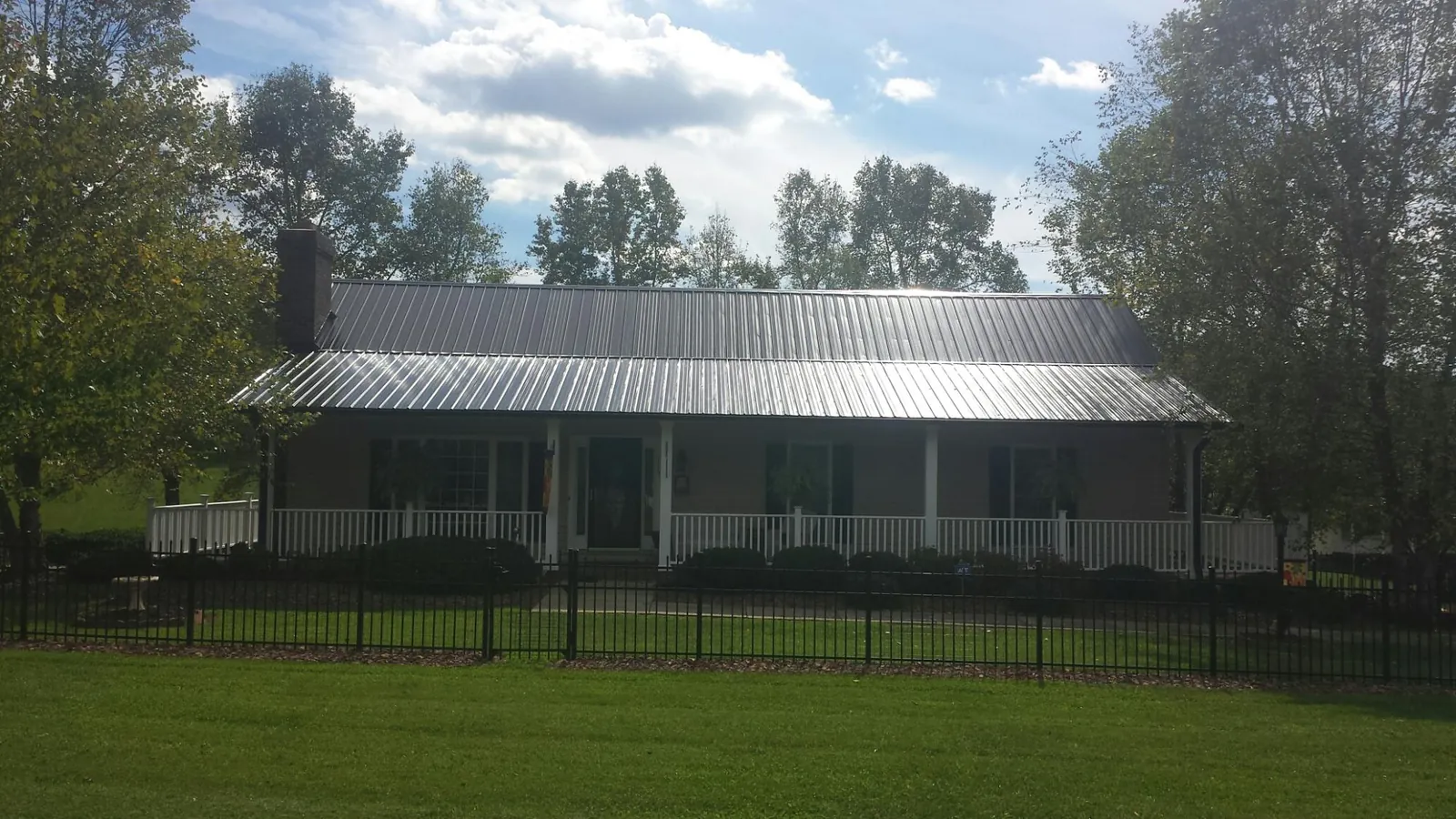 Gray metal roof on a brick ranch with a full width front porch — Gutter Guard Installation work by our crew in Edmeston