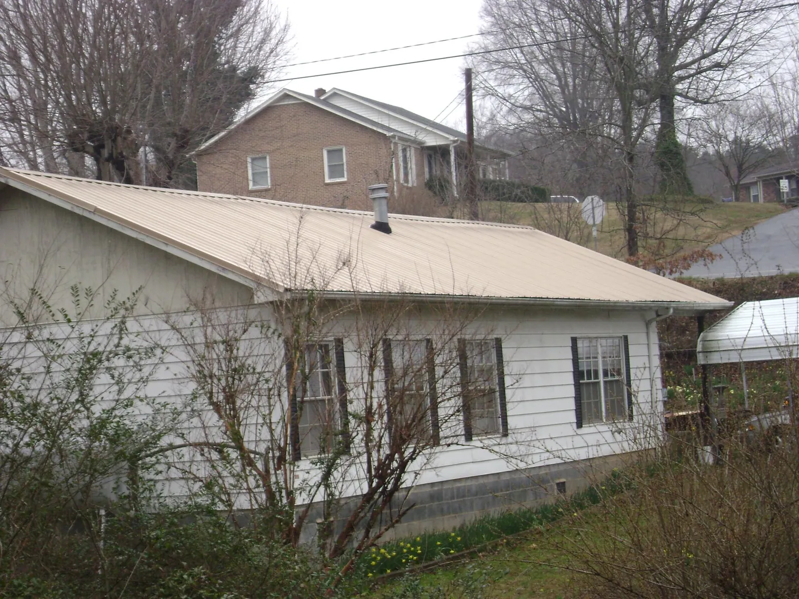 Tan metal roof on a white sided house set into a hillside — Commercial Roofing by Roofing Brothers in Edmeston