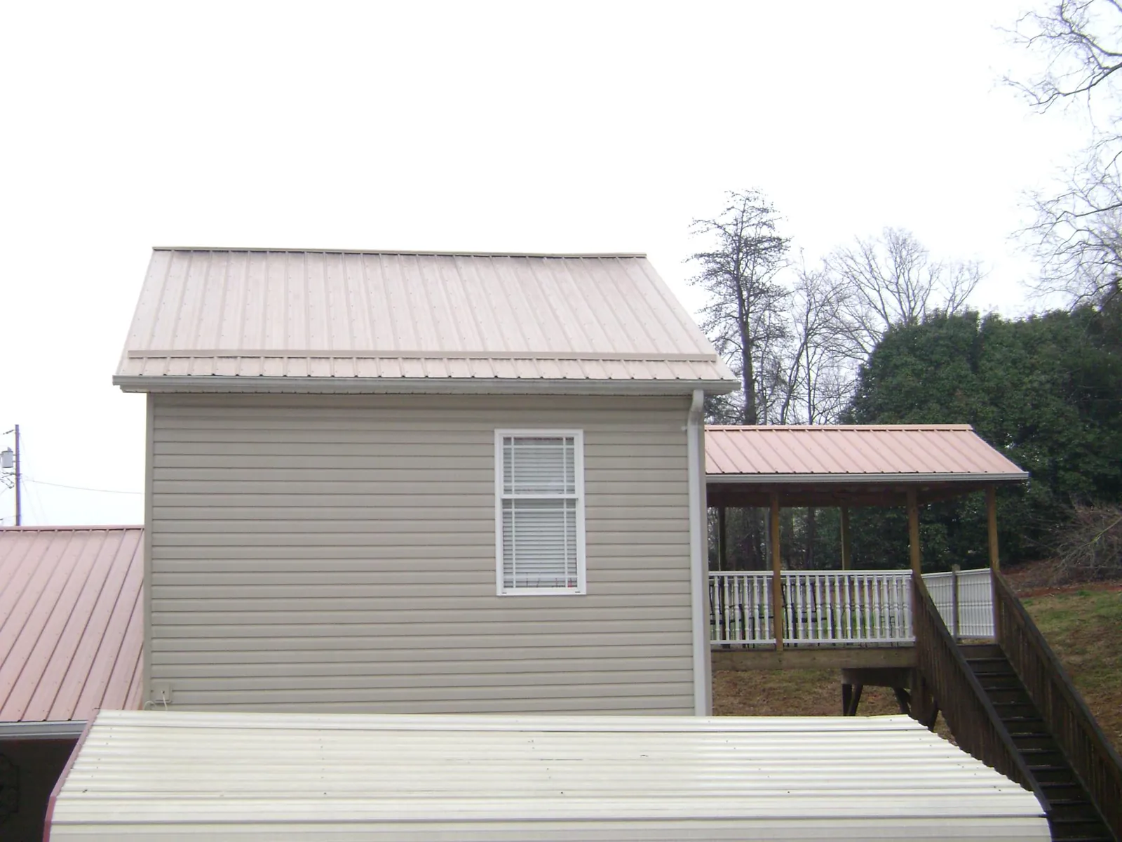 Tan metal roofs on a two story addition and attached porch, from a Roof Replacement job in Edmeston